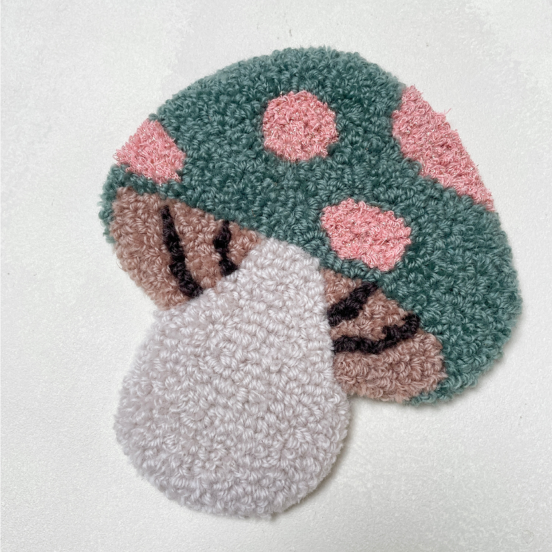 Tuftet svamp i blødt uldgarn med grønne og rosa detaljer. Ca. 18 x 17 cm og med filt på bagsiden. Håndlavet vægpynt fra Flair.