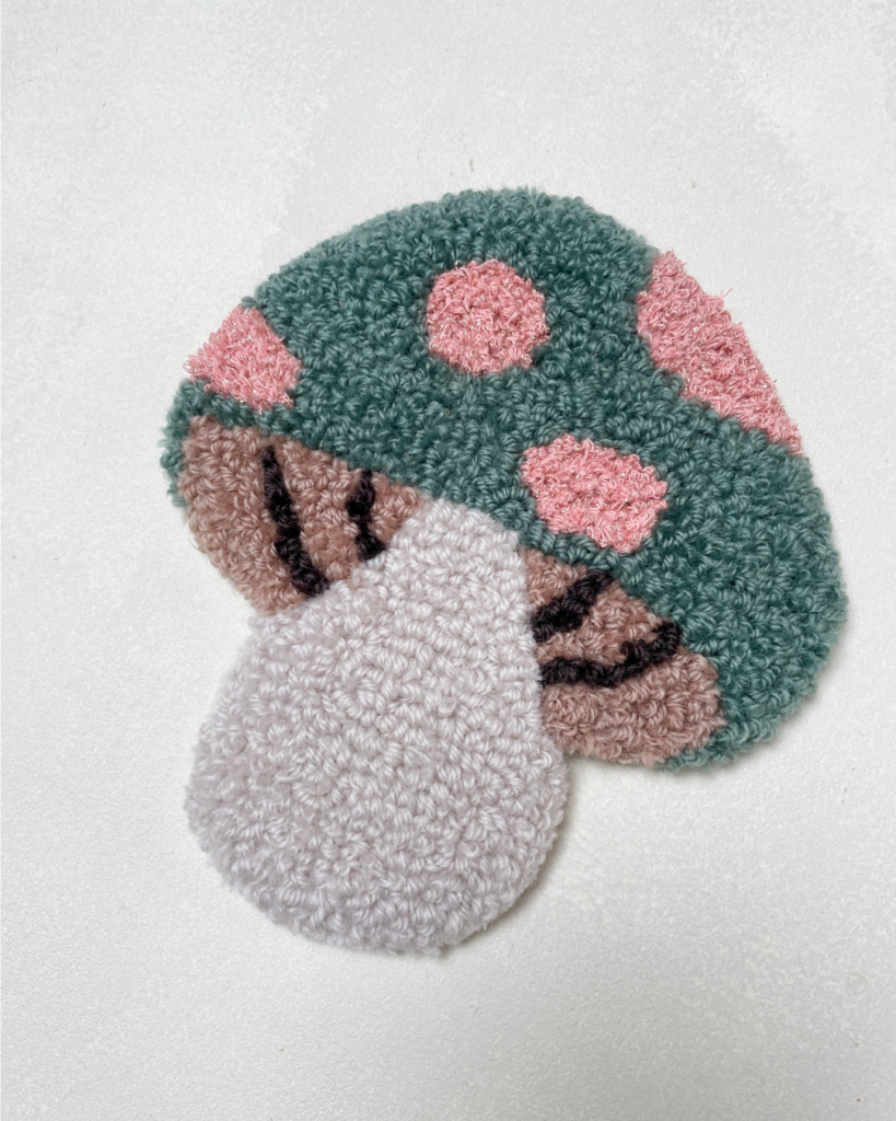 Tuftet svamp i blødt uldgarn med grønne og rosa detaljer. Ca. 18 x 17 cm og med filt på bagsiden. Håndlavet vægpynt fra Flair.